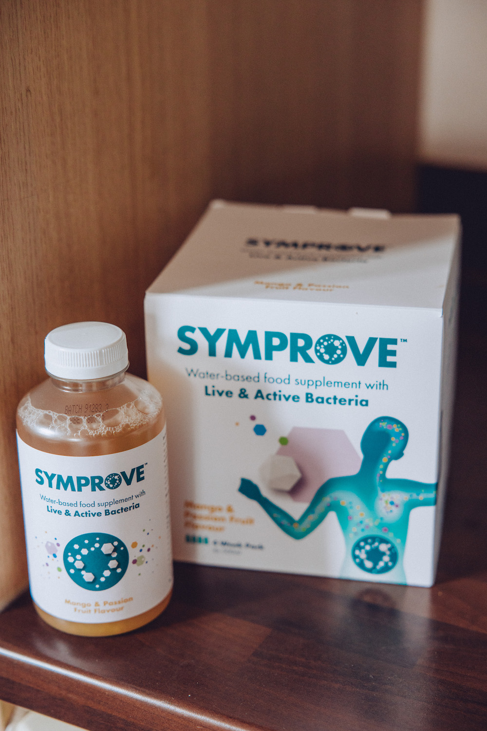 Bottle of mango and passion fruit of simprove probiotics with the box behind, sitting on a kitchen counter 